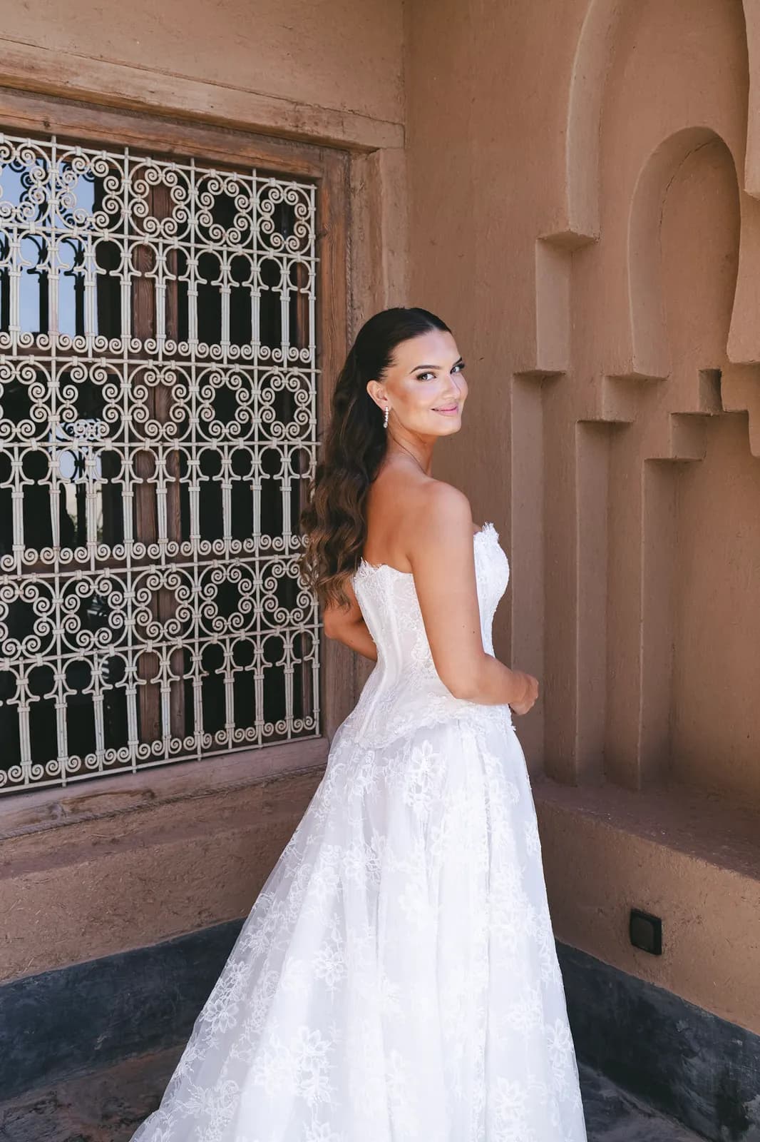 Bride beside a carved adobe niche and wrought-iron window at a Marrakech kasbah