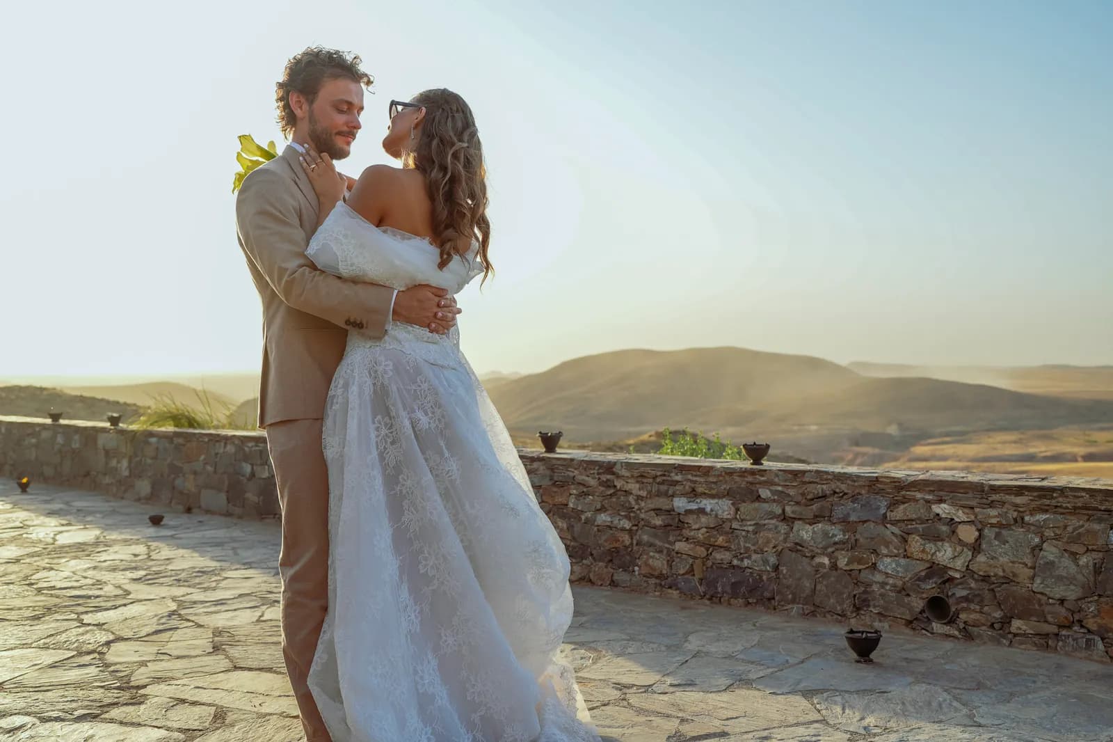 Newlyweds embracing on a desert terrace as the sun sets over Agafay