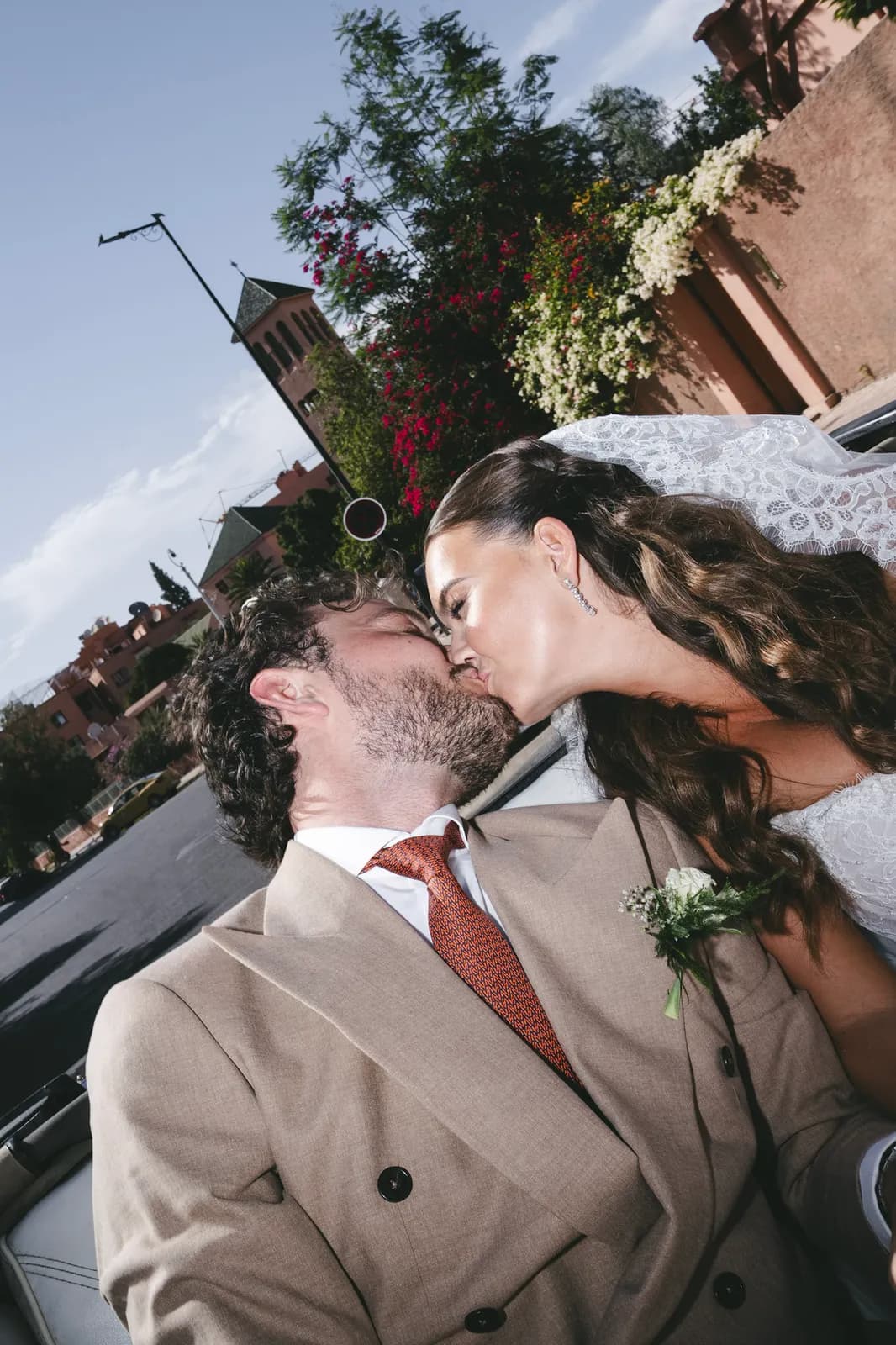 Bride and groom kissing on a Marrakech street lined with bougainvillea