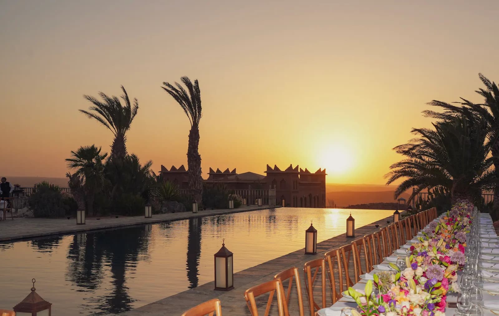 Sunset wedding dinner beside the infinity pool with palms and a kasbah at Agafay