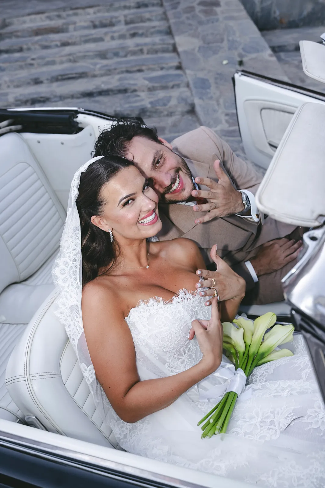Newlyweds laughing in the seats of a vintage convertible with calla lilies