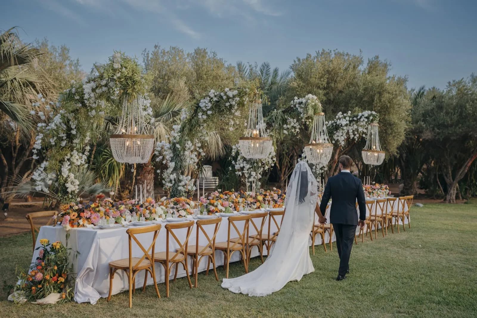 Bride and groom walking hand in hand toward their floral reception table in a Marrakech garden at golden hour